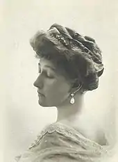Photo en buste et de profil d'une femme à la chevelure abondante retenue par des peignes et arborant des boucles d'oreille en perles blanches.