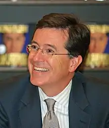 gros plan de Colbert, riant. Derrière lui, on aperçoit son livre exposé.