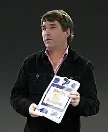 Photo d'un homme debout tenant entre ses mains un ouvrage papier.