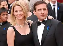 Photo d'une femme blonde, à droite, regardant à gauche de la caméra, et d'un homme brun, à gauche, regardant à droite de la caméra. Les deux sont enlacés et la femme a sa main posée sur l'épaule de l'homme.