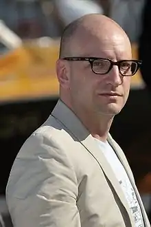 Photographie d'un homme avec des lunettes habillé en costume blanc.