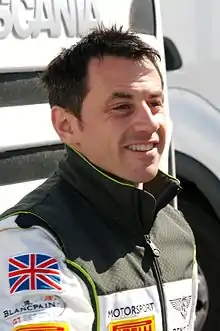 Photographie d'un homme blanc, brun, vue de trois-quarts droit en plan poitrine, souriant, avec des vêtements blancs et vert foncé aux couleurs de Bentley.