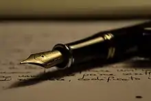 Un stylo noir à plume dorée, posé sur une feuille couverte d'écritures manuscrites.