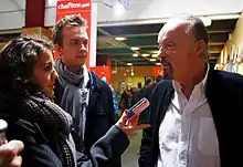 Deux étudiants de l'institut de Rennes interviewent Alan à droite à l'aide d'un téléphone aux couleurs du drapeau américain.