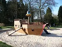 Portique de jeu à thème au sein d'un bac à sable, le bateau est creux et constitue une maisonnette d'enfant.