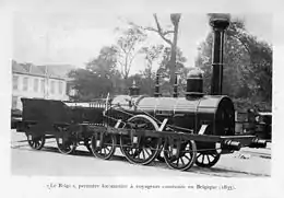 Photographie de la locomotive à vapeur « Le Belge ». On distingue son imposant corps de chauffe riveté, coiffé d'une cheminée, ses grandes roues à rayon. L'attelage comporte également à sa suite le tender : sa réserve en eau et charbon