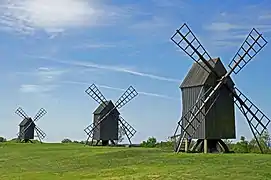 Trois moulins à vent quasi-identiques en bois alignés dans un paysage ouvert.