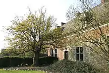 Photo d'un vieil arbre dans le jardin d'une riche ferme ancienne de brique et de pierre à toit d’ardoise et chiens-assis.