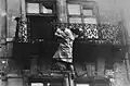 Une femme s’accroche à un balcon, se préparant à sauter dans la rue où les SS l’attendent.
