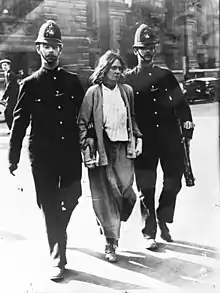 photographie en noir et blanc d'une suffragette est arrêté par deux policiers anglais qui la tiennent par les bras