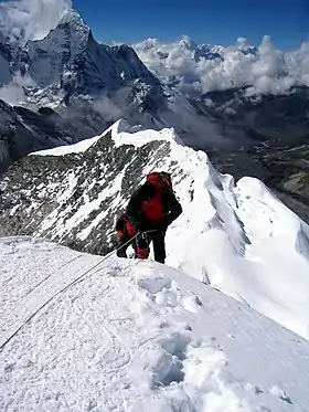 Deux alpinistes encordées terminant l'ascension d'une arête neigeuse et la vallée en contrebas, en arrière-plan.