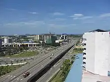Photographie d'une route à trois voies traversant une ville moderne et tropicale.