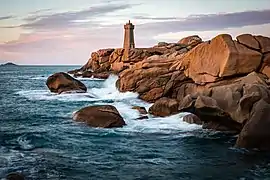 Côte rocheuse bordée par la mer, avec un phare visible au loin.