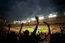 Cinq avions militaires américains survolent un grand stade sous les acclamations de tout un public.