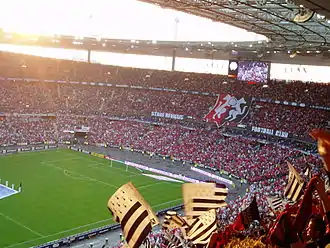 Photographie montrant la tribune d'un stade, avec un blason de grande taille en tissu, déployé par la foule.