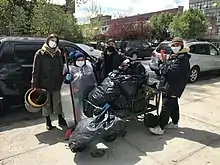 Photographie d'un groupe de personnes masquées entourant un chariot contenant des sacs poubelles pleins.