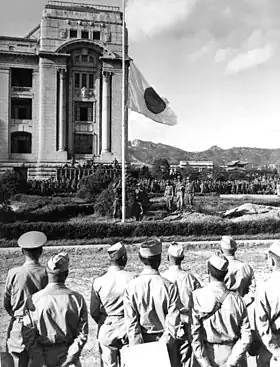 Des hommes en habit militaire regardent un drapeau qui est en train d'être baissé.