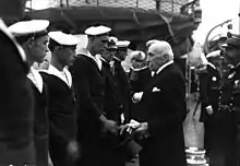 Photographie en noir et blanc d'un civil serrant la main de marins placés en ligne.