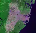 Image satellite (Landsat 7) de Sydney et de ses banlieues environnantes. L'image montre comment les zones bâties (en rose) ont été contraintes par la Royal National Park au sud, le parc national de Ku-ring-gai Chase au nord, et le parc national des Blue Mountains à l'ouest (une limite qui suit généralement une structure géologique appelée le Monocline de Lapstone, divisant les Blue Mountains de la plaine de Cumberland).