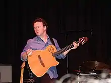 Homme sur scène avec une guitare acoustique.