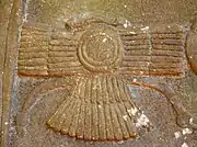 Disque muni d'ailes et d'une queue d'oiseau, VIIIe siècle AEC. Stèle de Bel-Harran-beli-usur, Irak. Ce symbole figure déjà sur un bas-relief babylonien, une borne, qui date du règne de Marduk-balassu-iqbi (r. 818-813 AEC). Musée de l'Orient ancien, Istanbul