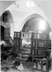 Photo d'archive en noir et blanc de l'intérieur d'une synagogue, avec au sol des traces de saccage.