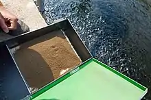 Distributeur de granulés. Les granulés se trouvent sur un tapis roulant qui avance lentement mais régulièrement poussant les granulés dans l’eau.