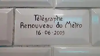 Carreau blanc biseauté indiquant la date de rénovation de la station en lettres manuscrites.