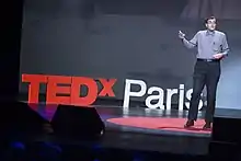 Photo d'un homme debout, faisant un discours devant un panneau indiquant TEDEX Paris.