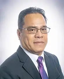 Homme en costume gris sombre à cravate violette portant de fines lunettes