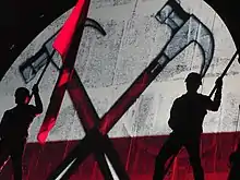 Deux marteaux sur un fond rond rouge et blanc projeté sur un mur. Deux gardes avec des drapeaux en main bloquent légèrement la vue.
