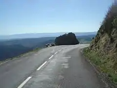 A quelques hectomètres du sommet, la grande table d’orientation à côté d’un rocher. Panorama vers le parc national des Cévennes au fond.