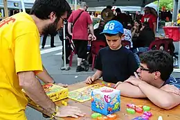 Table de jeux lors de la 1re édition du Brussels Games Festival où un animateur explique un jeu à deux personnes