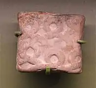 Petite tablette carrée en argile avec des motifs circulaires imprimés sur sa surface.