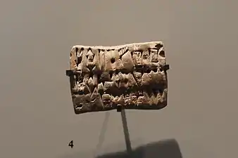 Tablette en argile ébréchée, divisée en lignes comprenant des signes proto-élamites et numériques.