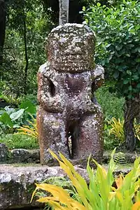 Photo d’une statue de tiki en pierre de deux mètres cinquante de haut. Le bras gauche est manquant.