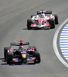 Photo d'une monoplace rouge et bleue devançant une autre monoplace blanche et rouge en piste