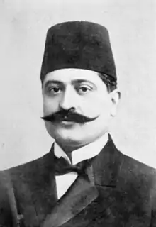 Portrait d'un homme moustachu, en costume, nœud papillon et fez.