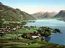 L'illustraton est une photographie ancienne colorisée. Elle montre un village accolé au lac d'Annecy. Tous les coteaux aux premier et deuxième plans sont couverts de vigne. En arrière-plan, les pentes fortes sont boisées.