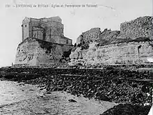 Photographie en noir et blanc du promontoire de Talmont surmontée de son église et entouré de remparts.