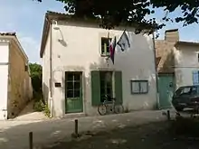 Photographie de la mairie de Talmont, petit bâtiment de style saintongeais abrité d'un tilleul et entouré de roses trémières