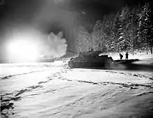Photo noir et blanc d'un char dans la neige, en train de tirer.