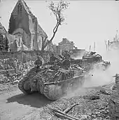 Au milieu des ruines, un char de dépannage Sherman Recovery, remorquant un Sherman de combat hors de service, traverse Bourguébus pendant la bataille de Normandie.