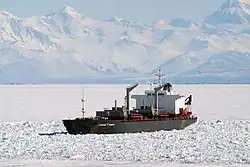 Bateau entourée de glace de mer devant une chaîne de montagnes imposante.