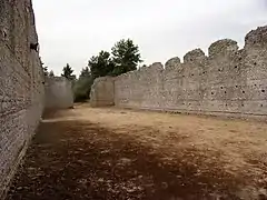 Photographie en couleurs de l'intérieur non cloisonné d'une vaste bâtiment aux murs ruinés en partie haute.