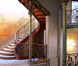 Photo en couleur d'un palier avec colonnes fines, mosaïque au sol, arabesques sur la rampe d'escalier et les murs