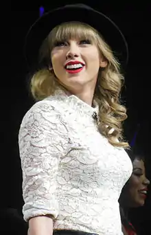 Taylor Swift wearing a brimmed hat and a laced white shirt smiling