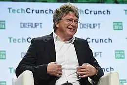 Photo d'un homme souriant et portant des lunettes sur la scène d'une conférence.
