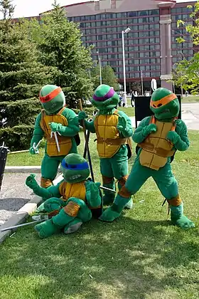 photo en couleur de 4 personnes déguisées en tortues masquées et tenant des armes japonaises (sai, bo, ninjato et nunchakus)