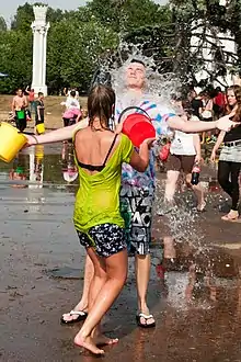 Une adolescente envoie un seau d’eau au visage d’un adolescent, pendant une bataille d’eau